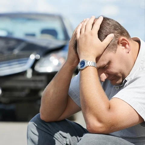 Auto Injury Auburn WA Man Sitting A man sitting in front of a car after a car accident.